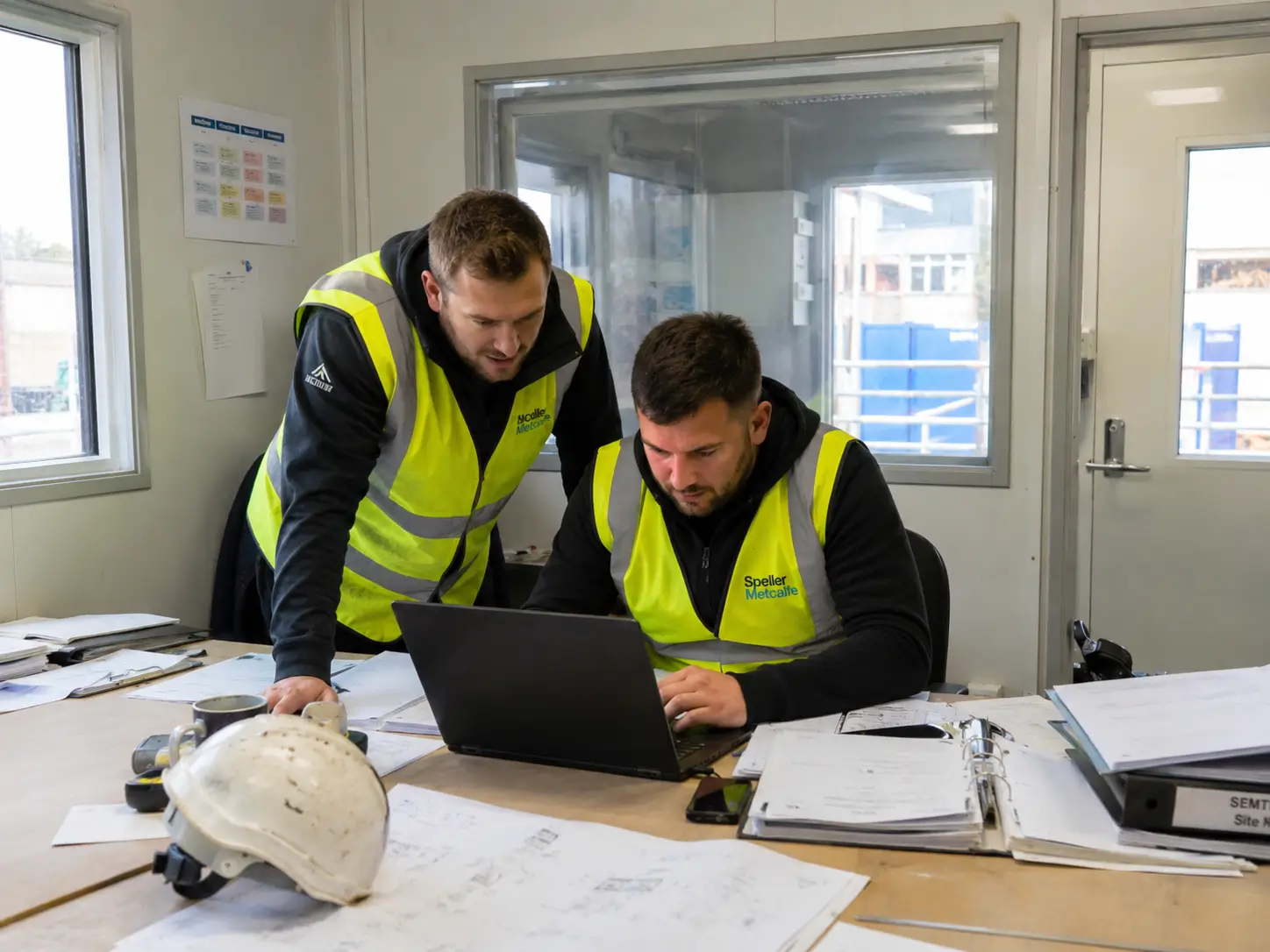 Construction site manager reviewing NVQ assessment costs on a live site