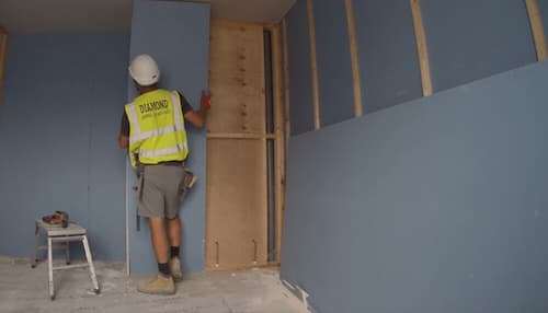 Boarder tacking plasterboard sheet to the wooden frame in the workplace